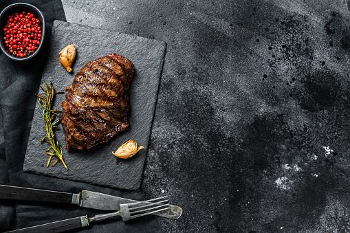 Grilled Flat Iron steak on a stone Board, marbled beef. Black background. Top view. Copy space.