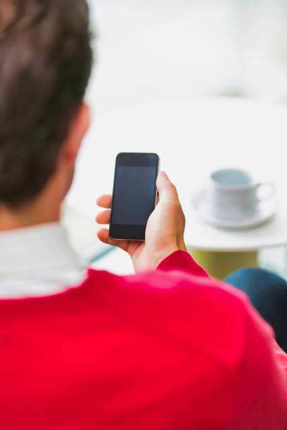 istock Rear view of businessman using smartphone while sitting and drinking coffee in lobby 1221990647