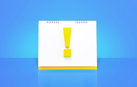 Monthly yellow desk calendar with exclamation point on blue background. Horizontal composition with copy space. The calendar is yellow in color and standing on a desk over blue background. Front view.