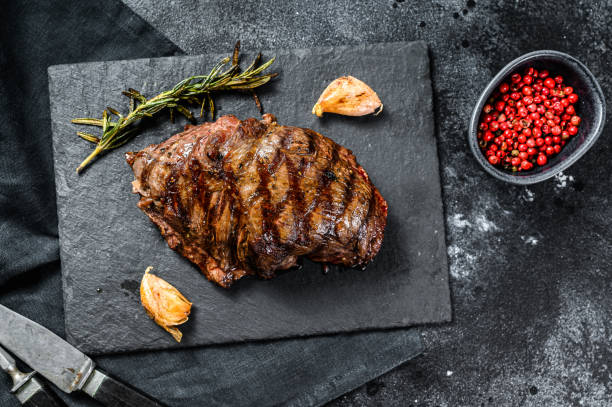 istock Grilled Flat Iron steak on a stone Board, marbled beef. Black background. Top view 1221992847