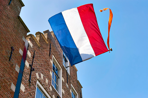 Dutch flag with orange streamer waving in the wind on the facade of a typical dutch house with stepped gable on Koningsdag. A national holiday in the Kingdom of the Netherlands.