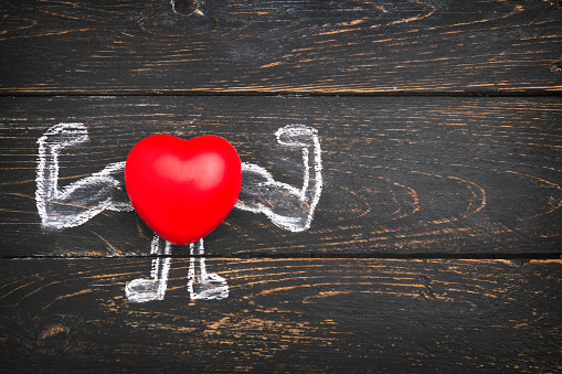 Heart with muscular arms drawn on wooden background