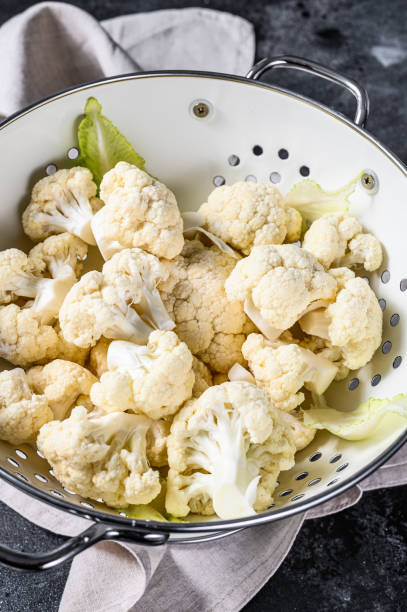 istock Washed fresh cauliflower cut into pieces in a colander. Black background. Top view 1221995977