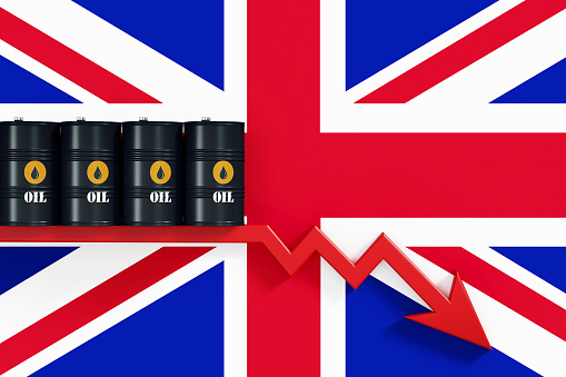 Black oil barrels sitting over a red arrow that is moving down on British flag. Horizontal composition with copy space. Global Oil industry supply and demand concept.