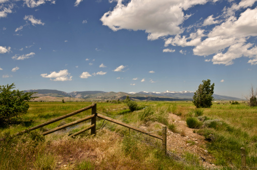 Combination of wood and barbed wire fending mark the boundary of a ranch with a view of mountains that still have snow on a beautiful, windy summer day in Montana