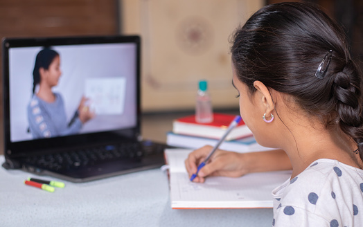 Concepto de educación en casa o e-learning, jovencita ocupada en la escritura mirando en la computadora portátil mientras que la profesora explica durante la crisis de la pandemia de covid-19 o coronavirus. photo