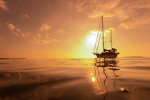 Luxury sailing yacht in front of beautiful golden incredible sunset in tropical ocean. Romantic trip. Summer holiday vacation travel concept. Selective focus.