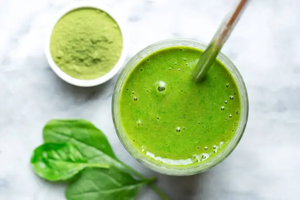 Overhead and close-up view of a homemade spinach smoothie with Moringa powder and a stainless steel drinking straw