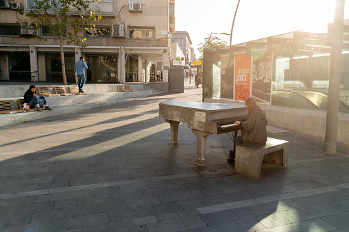 Haifa, Israel-November 25, 2019. Young Girl plays music on the piano outdoors in the Haifa street lit by the rays setting sun