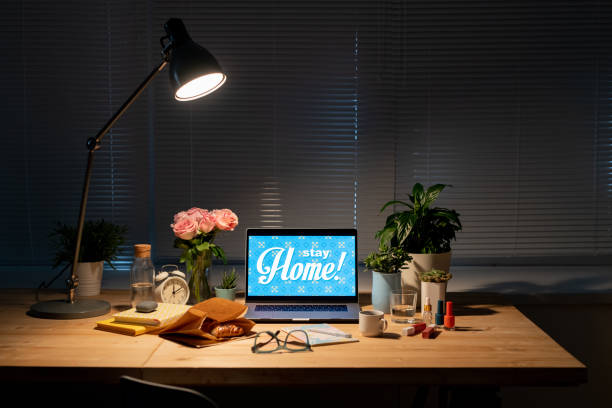 istock Workplace by window in dark room with items on table and lamp above them 1222006223