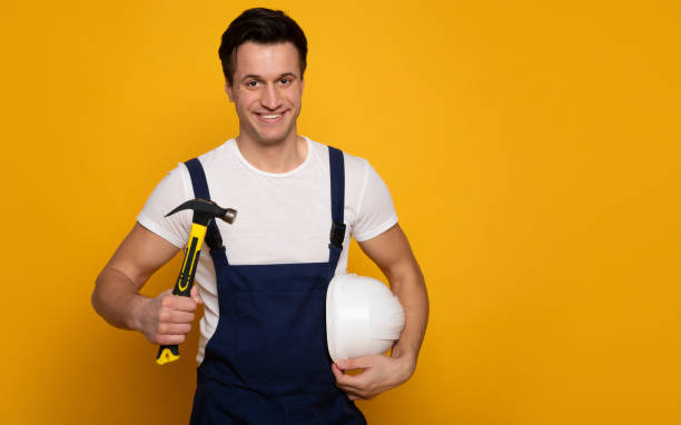 istock Builder worker. Close-up photo of a young builder worker, who is holding a hammer in his right hand and a white helmet in his left hand, while looking in the camera and smiling. 1222011682