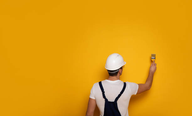 żółta farba. zbliżenie zdjęcie mężczyzny w garniturze roboczym i białym kasku, który maluje ścianę w yelllow. - paint brushing house painter wall zdjęcia i obrazy z banku zdjęć