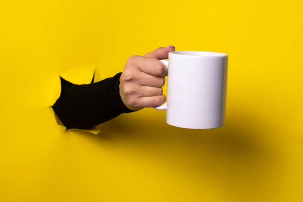 istock Hot drink concept.Hand holding mug from a torn hole in yellow paper 1222013773