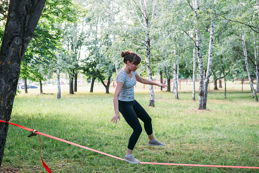 Young woman slacklining in summer park