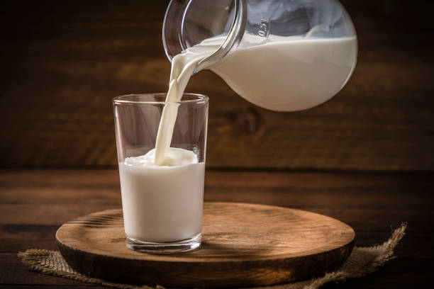 Pouring milk into a drinking glass Front view of a pitcher pouring milk into a drinking glass on a rustic wooden background. Low key DSLR photo taken with Canon EOS 6D Mark II and Canon EF 24-105 mm f/4L milk stock pictures, royalty-free photos & images