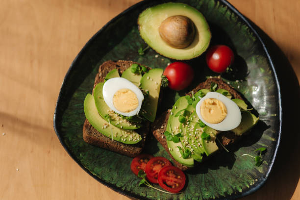 istock Delicious breakfast at home. Sandwich with fresh sliced avocado above rye bread with cherry tomatoes and boiled egg on green plate. Top view 1222019884