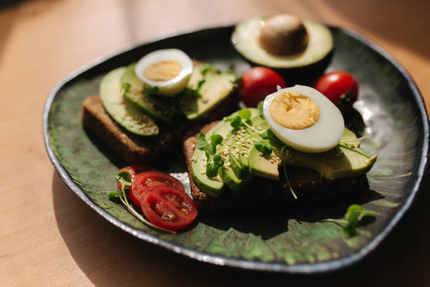 istock Delicious breakfast at home. Sandwich with fresh sliced avocado above rye bread with cherry tomatoes and boiled egg on green plate 1222019886