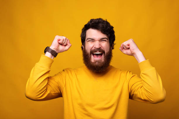 istock Strong bearded man is making the winner gesture with both hands on yellow background. 1222021381