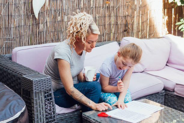 Show Me Again A young Caucasian girl sits on the sofa in the back garden with her mum doing her schoolwork. love me again stock pictures, royalty-free photos & images