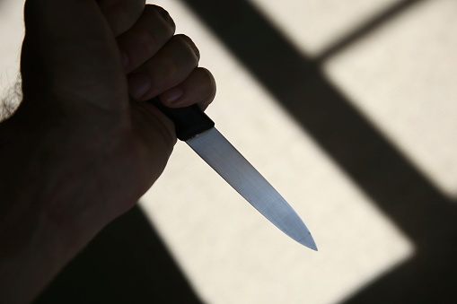 A hand holding a knife in shadow. This image can be used to represent stabbing or murder.