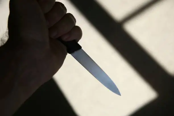 Photo of A hand holding a knife in shadow. This image can be used to represent stabbing or murder.