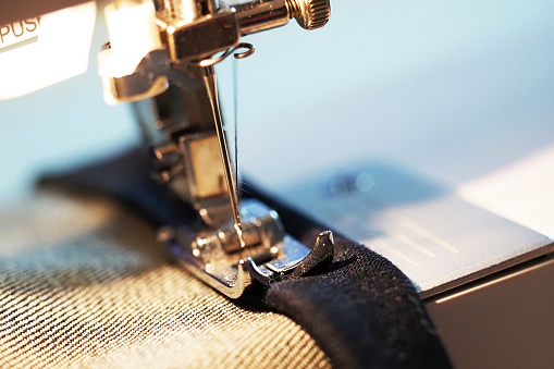 Sewing machine. Tailor working, hem the dark blue jeans, macro