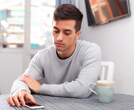 Young man is sad sitting with phone because she is alone at home