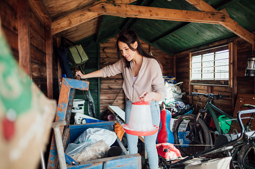 Woman collecting tools in a shed ready to work outdoors. She is opening up a container and looking inside.