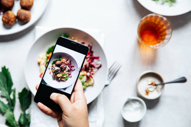 Chef taking photograph of vegan falafel bowl on table. Hand of a chef taking photograph of vegan falafel bowl on table with a mobile phone. Hand of cook photographing meal. plate photos stock pictures, royalty-free photos & images