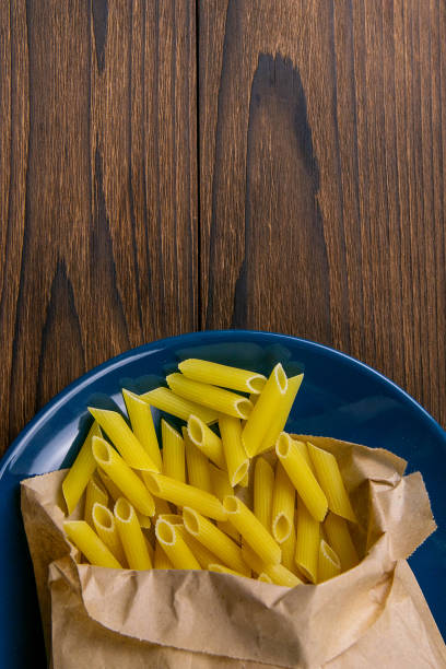 Pene Lisce pasta in a craft paper bag on a blue plate on a wooden table. Top views with clear space