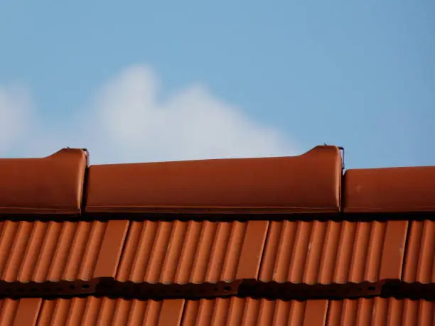 sloped red clay tile roof and ridge. blue sky and white cloud. construction, modern building materials and technology concept. abstract low angle close-up view.