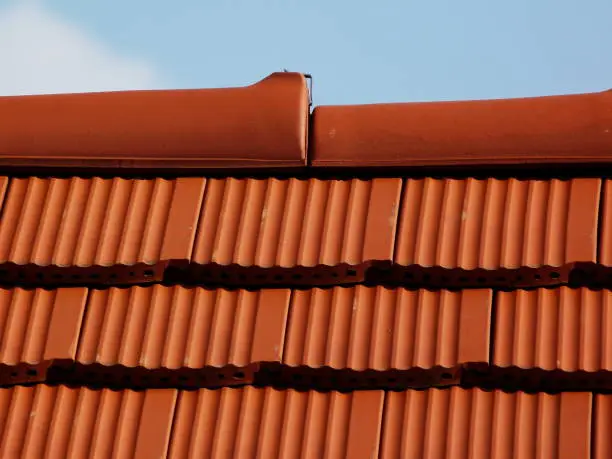 sloped red clay tile roof and ridge. clear blue sky in day light. construction, modern building materials and technology concept. abstract low angle view.