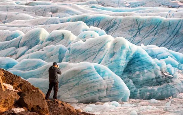 Man photographs the blue glacial ice at the Svinafellsjokul glacier in southeast Iceland. This is the largest ice cap in Europe.