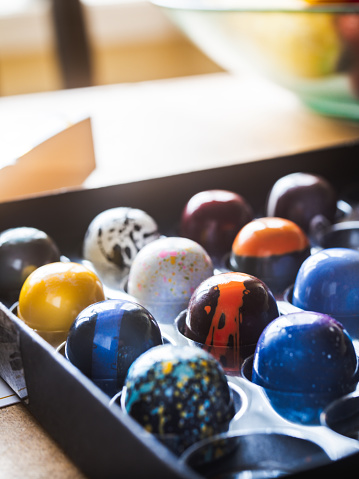 Box of artisanal chocolate on wooden table in kitchen of a home. Bowl of fruit in the background, out of focus.