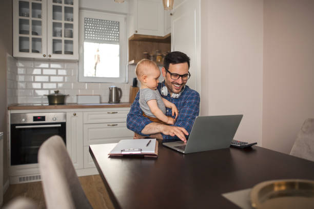 istock A father working remotely on a laptop while holding his baby boy. 1222044094