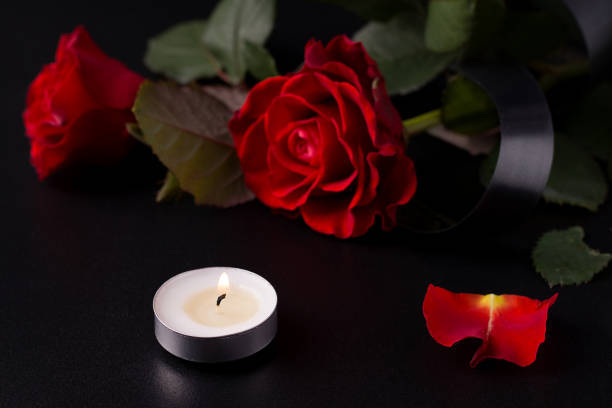 istock The concept of death, sorrow and loss. Red roses on a black background next to candles 1222052257