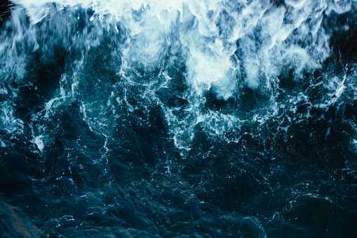 Rough stormy blue ocean waves with white foam, aerial view.