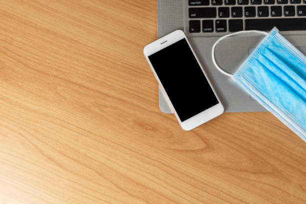 istock Work from home concept. Top view laptop, smartphone, and face mask on wood table with copyspace for text or design. 1222054511