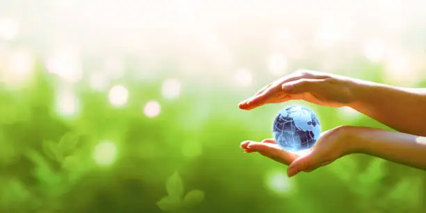 Photo of Card for World Earth Day. Blue planet crystal globe in human hand on green background. Saving environment, save, protect clean planet and ecology, sustainable lifestyle concept.