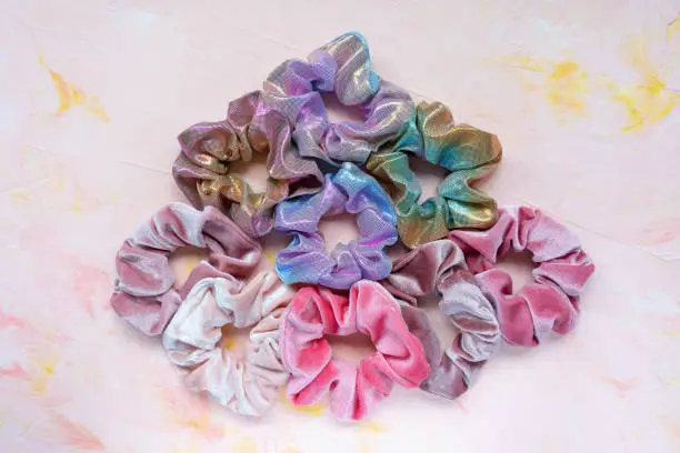 Trendy velvet and holographic iridiscent shiny metallic scrunchies on pink background. Diy accessories and hairstyles concept, copy space