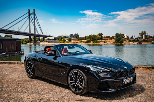 BMW Z4 convertible parked next to the river in Belgrade. Car is black color with orange interior. Photo is colorful with nice landscape in the background.