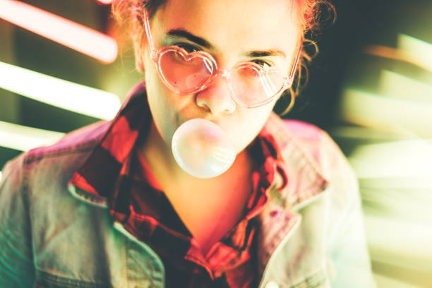 istock Millennial girl blowing bubble gum illuminated neon light. 1222069108