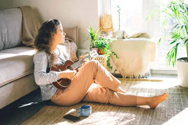 Photo of Young beautiful woman plays ukulele, sings in the sun.