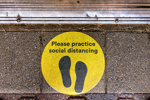 Above view for yellow warning sign to maintain social distance distancing during covid-19 coronavirus outbreak with footsteps on street