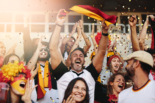Group of multi-ethnic people cheering their national team. German soccer team supporters enjoying during watching a match from stands.