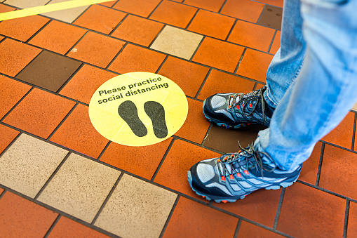 Yellow warning sign to maintain social distance distancing during covid-19 coronavirus outbreak with footsteps in store and legs of person in USA
