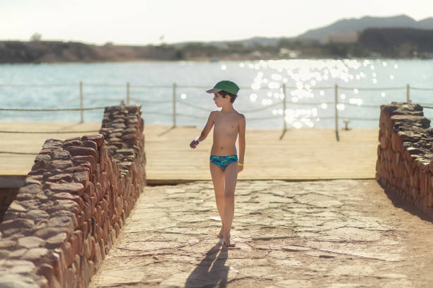 Boy in a swinsuit is standing by the beach
