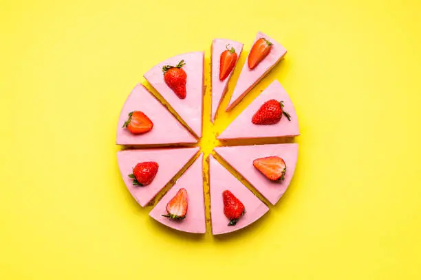 Strawberry cheesecake sliced in unequal pieces, on a yellow seamless background. Flat lay with no-bake strawberry cake. Berry gelatine creamy dessert