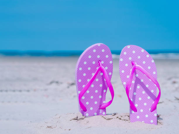 istock Summer composition with beach cccessories beach flip flops and colorful hat on tropical sand against blue sea and sky background. summer vacation concept of beach holiday, sea tour, warm sunny summer. 1222075353