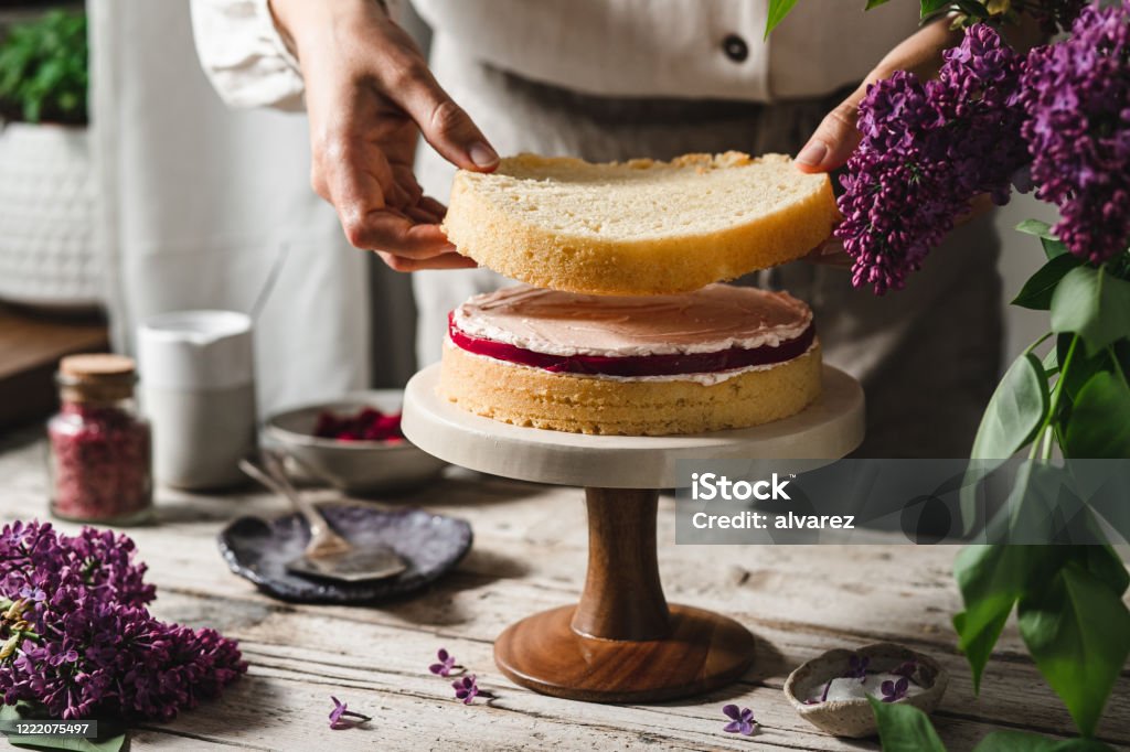Close-up of female chef preparing layered cake Close-up of female chef preparing cake. Woman making a layer cake with ingredients on table. Cake Stock Photo